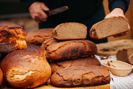 hands with bread man is cutting dark bread with knife	