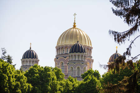 View Of Riga Nativity Of Christ Cathedral with golden yellow domes - Famous Church And Landmark in Summer day. Riga, Latvia. Riga Cityscape surrounded with trees on blue sky background.の写真素材