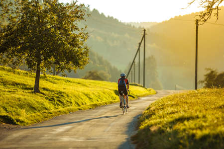 Male fully equipped cyclist riding a bike during sunset on the empty road in rural Germany.の写真素材