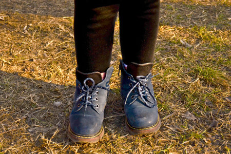 A little girl in autumn shoes walks in the park. Blue boots close-upの写真素材