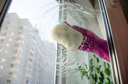 Womens hands in rubber gloves wash the window with sponge and foam. housework and cleaning conceptの写真素材