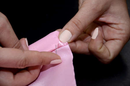 Woman's hands with a pin stab the fabric. Tucked up a pink cloth. Preparation for sewing curtains on a black table in the studio. Small business concept.の写真素材