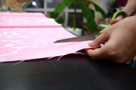 Cutting pink fabric in a sewing workshop on a black table. Cutting pink fabric in a sewing workshop on a black table. Preparing for sewing curtains. Cutting with light green tailor scissors. small business.の写真素材