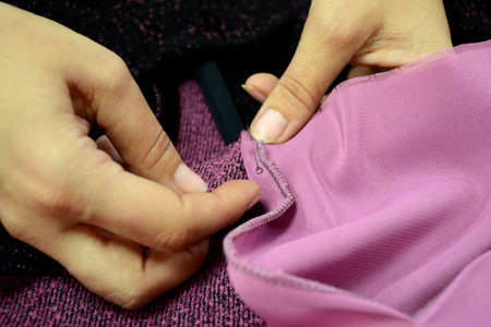 Seamstress prepares knitwear for sewing clothes. Female hands with a pin stab black and pink fabric on the sewing table. small business.の写真素材