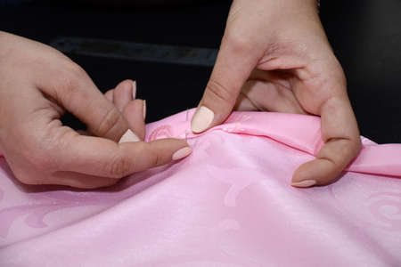Woman's hands with a pin stab the fabric. Tucked up a pink cloth. Preparation for sewing curtains on a black table in the studio. Small business concept.の写真素材