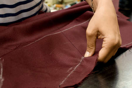 Women's hands sew maroon fabric with a needle. Seamstress in the workplace, small business concept.の写真素材