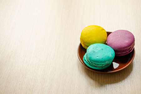 Macaroons on brown saucer on a wooden table, copy space