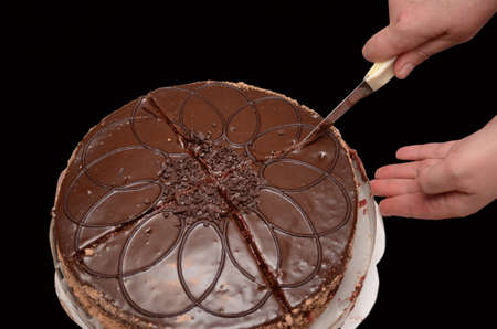 Hand with a knife cuts a chocolate cake closeup. Cake on a black background, isolated