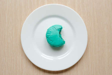 Bitten blue macaroon cookies white plate on wooden background, flat layの写真素材