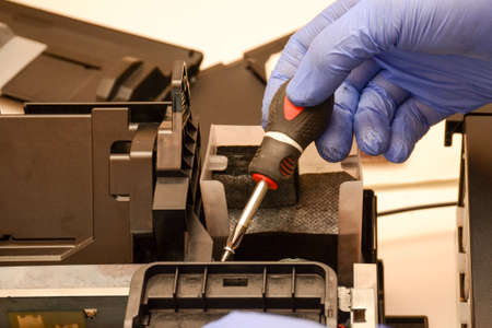 A man with screwdriver assembles a printer. Repair office equipment