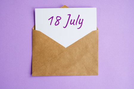 Kraft envelope with a white sheet of paper and the inscription July 18 on lilac background. Correspondence calendar and memorable date conceptの写真素材