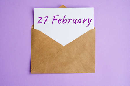 Kraft envelope with a white sheet of paper and the inscription February 27 on lilac background. Correspondence calendar and memorable date conceptの写真素材