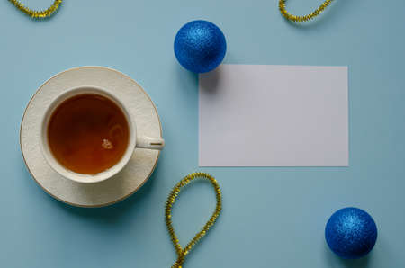 White cup with hot tea among shiny balls and gold tinsel on blue background. Christmas concept with copy space, flat lay.の写真素材
