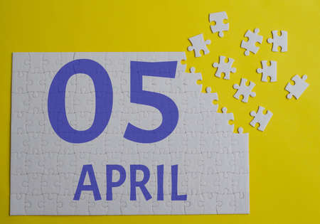 April 5 calendar date on a white puzzle with separate details. Puzzle on yellow background with blue inscriptionの写真素材