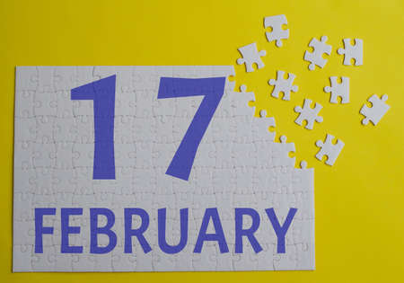 17 february calendar date on a white puzzle with separate details. Puzzle on yellow background with blue inscriptionの写真素材