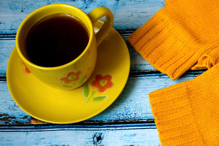 Yellow cozy knitted sweater with cup of coffee on a blue wooden table, top viewの写真素材