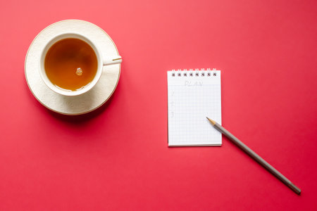 White cup with hot tea, notebook with blueprint and pencil red background, flat lay.の写真素材