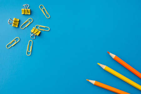 Orange and yellow pencils with paper clips on a blue background, flat lay. Blank copy spaceの写真素材