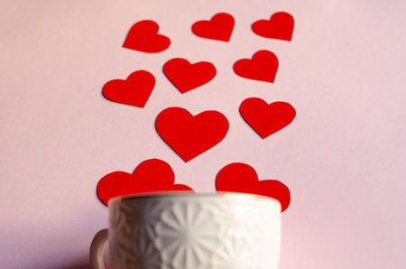 Red hearts are falling from white mug on a pink background, horizontal photo close-up. Valentine's day, wedding and love conceptの写真素材