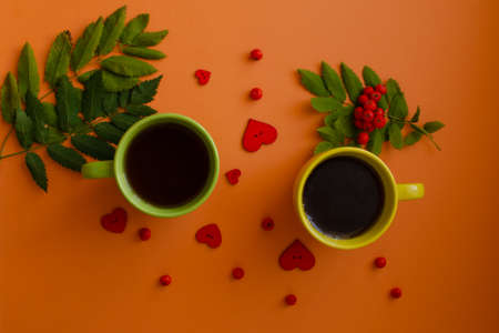 Yellow and green mugs with ripe rowan berries and red hearts on an orange background flat layの写真素材