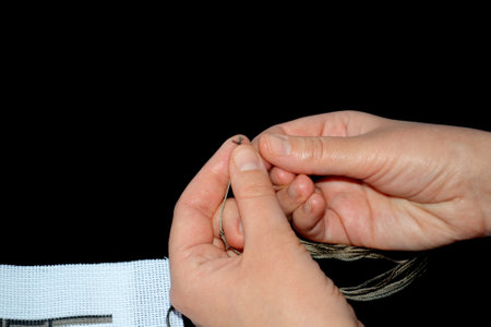 cross-stitch. Needle for embroidery in female hands. White fabric with pattern. The pattern is...