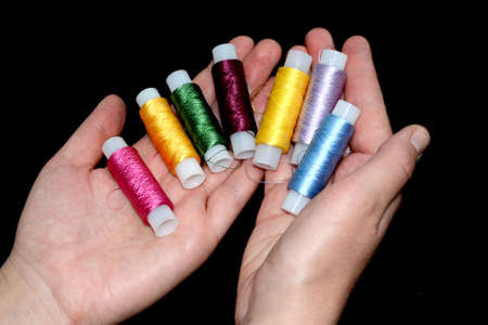Female hands hold skins of thread. Silk threads for embroidery. Skeins of yellow, blue, green pink,...