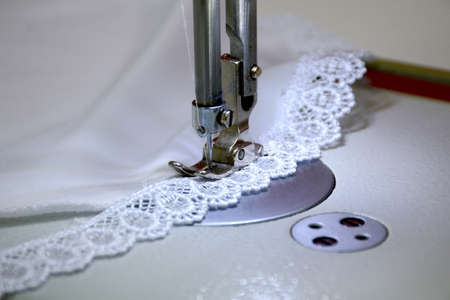 Sewing a white satin fabric, stitching lace on a sewing machine. Small business concept.