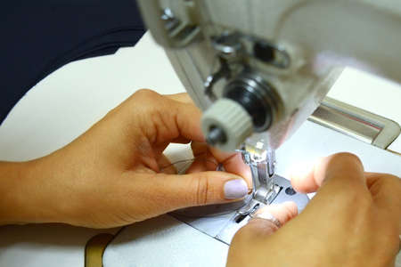 Female hands insert a dark thread into the needle of a white sewing machine. Small business concept....