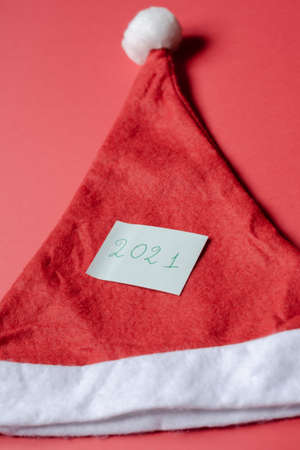 The inscription on the sheet 2021 on hat of santa claus. Hat on red background, Christmas and New Year conceptの写真素材