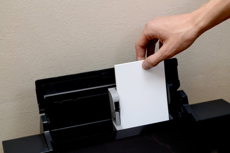 A male hand inserts white paper for printing photos into a black printer.