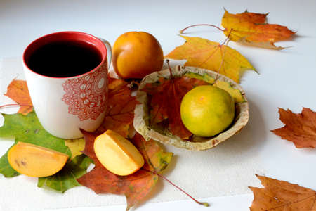 A colorful photo of autumn maple leaves, a mug of tea and citrus fruits on the table. Horizontal autumn photo, food healthy conceptの写真素材