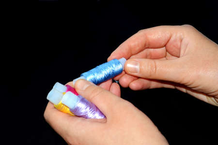 Female hands hold skins of thread. Silk threads for embroidery. Yellow, lilac and pink skeins in the...