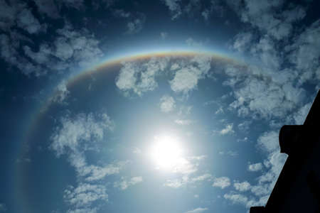 Rainbow halo in the blue sky with white clouds. Magic natural rainbow effect with the sun in the...
