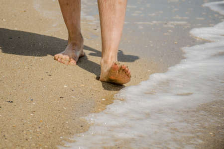 Men's feet go along sandy seashore. healthy lifestyle concept