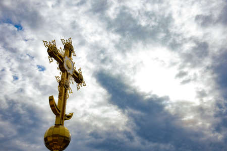 Cross on a background of the sky with gray clouds. Golden orthodox cross close-up. Religion concept,...