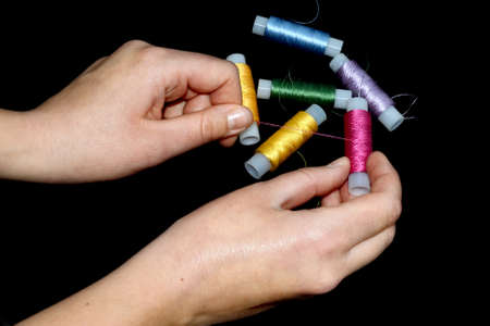 Female hands hold skins of thread. Silk threads for embroidery. Skeins of yellow, blue, green pink and lilac. Black background.の写真素材