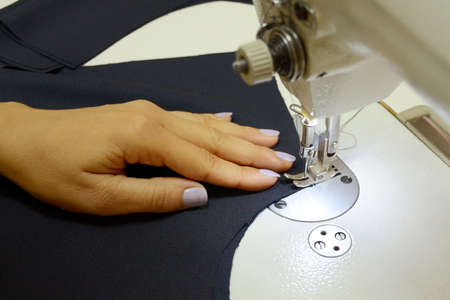Women's hands sew on a white sewing machine from a dark blue fabric. Small business concept....