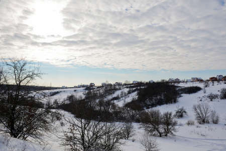 Winter landscape on a sunny day and with clouds. Gully and hill with residential buildings on the...