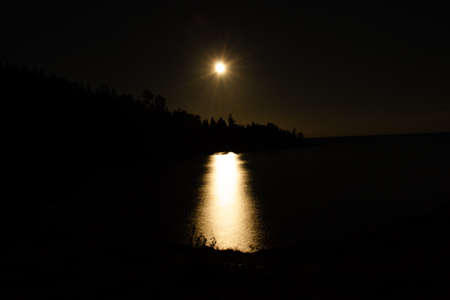 Moon trail at night it calm water of Ladoga lake among rocks, horizontal photoの写真素材