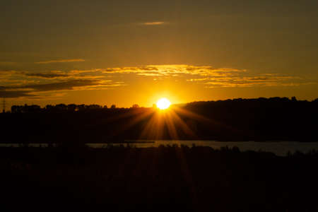 The sun is setting behind forest, beautiful orange and gold rays in the sky. Horizontal photo of a...