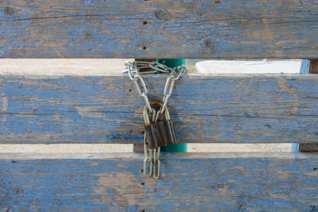 Padlock on a metal chain on the background of an old wooden fence, shabby pigeon paint