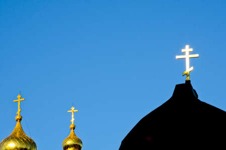 A golden Orthodox cross shines from the sun against a blue sky. Christian photo with copy spaceの写真素材