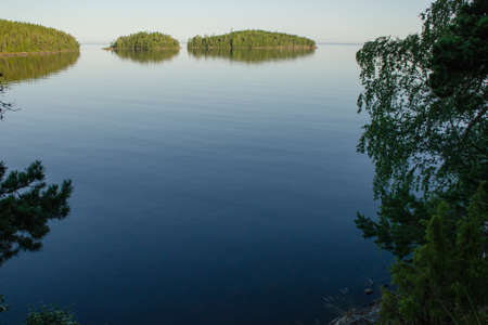 Islands with green forest in calm lake water against blue skyの写真素材