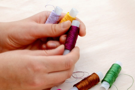 Female hands hold skeins of thread on a beige background. Silk threads for embroidery. Skeins of yellow, lilac, burgundy, green and brown. handmade concept.の写真素材