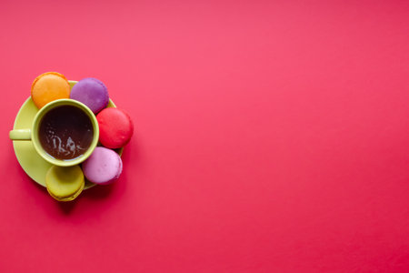 Colored macaroons and yellow cup of tea red background with copy space, flat layの写真素材
