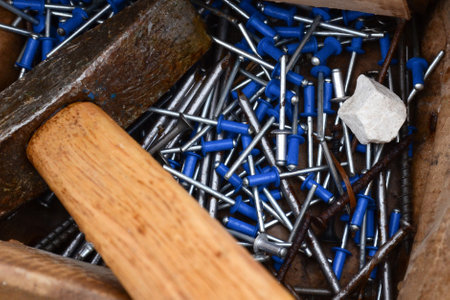 Old and new nails in an old box. New nails with a blue tip. Old hammer and white stone in a box close-up.の写真素材