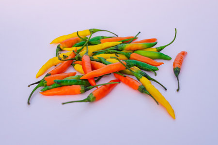 A bunch of colored hot chili peppers on lilac background. The concept of agriculture and organic...