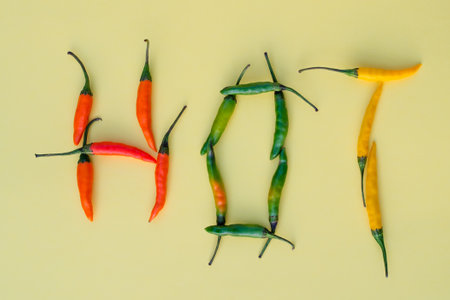 The inscription hot is made of colored hot chili peppers on yellow background in a flat lay.の写真素材