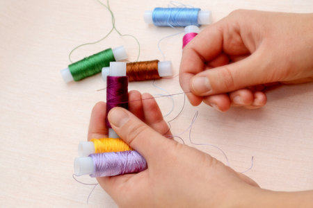 Female hands hold skeins of thread on a beige background. Silk threads for embroidery. Skeins of yellow, lilac, burgundy, green, pink, blue and brown. handmade concept.の写真素材