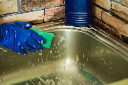 A woman in rubber gloves washes the sink with sponge and foam. House cleaning conceptの写真素材